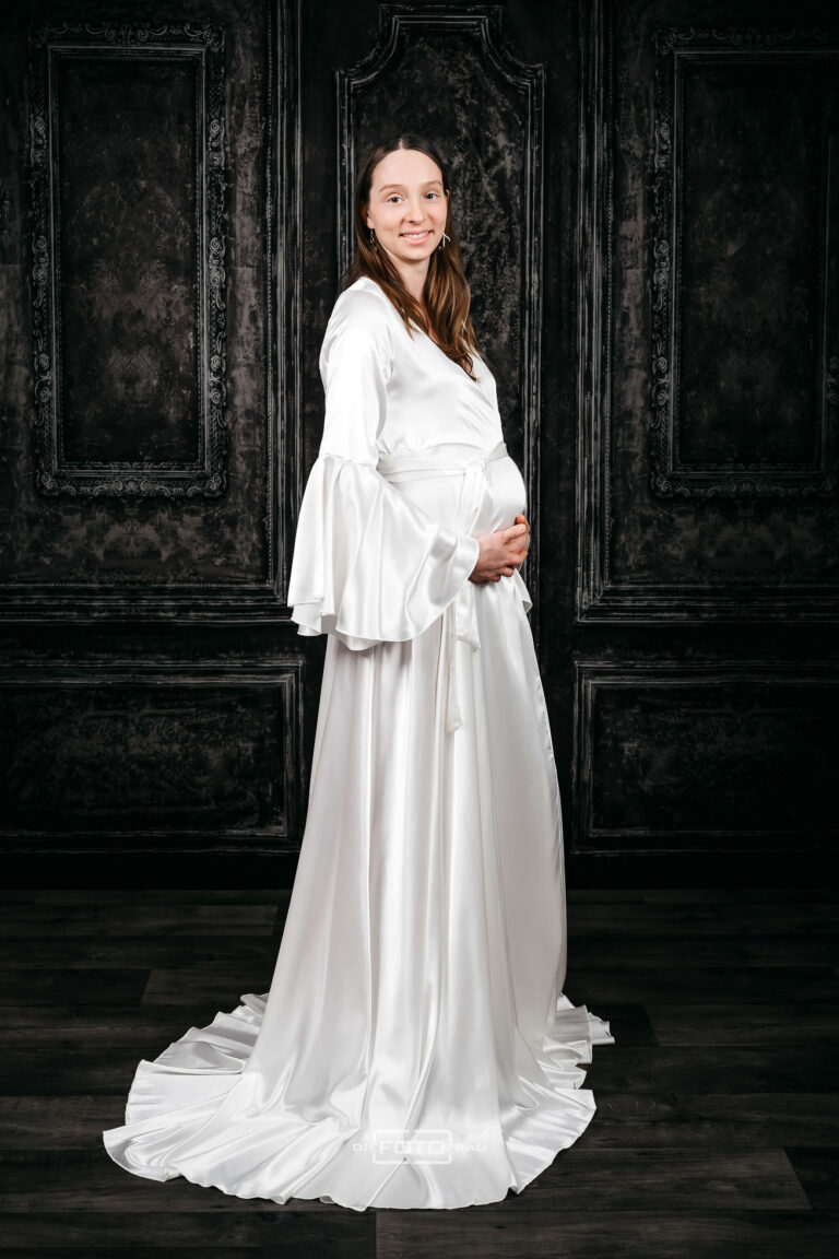 Babybauchshooting im Fotostudio, die werdende Mutter trägt eine weiße glänzende Babybauchrobe