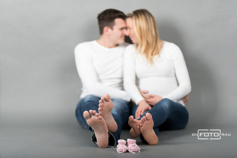 Babybauchshooting mit Fokus aus rosa Babyschuhe, das Elternpaar sieht man unscharf im Hintergrund