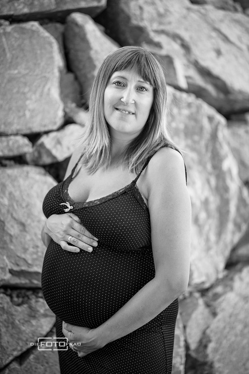 Babybauchshooting vor einer Steinmauer, das Bild ist schwarzweiss
