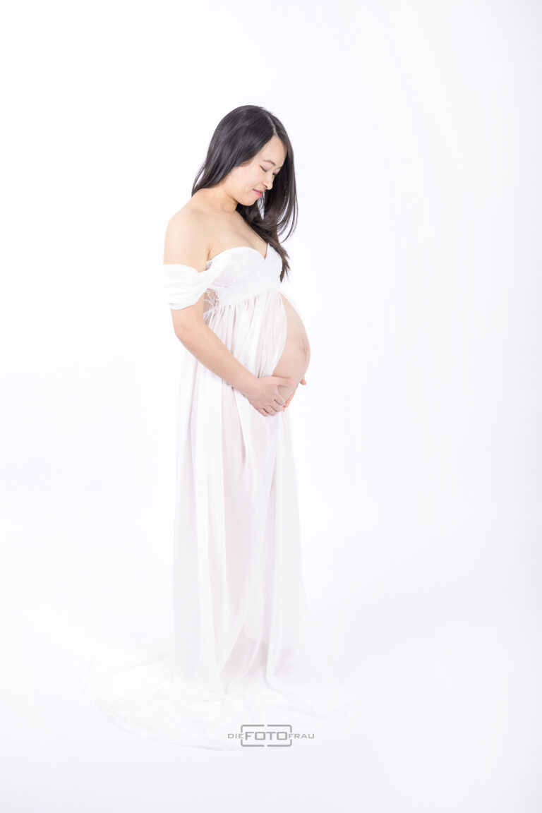 Babybauchshooting im Fotostudio, die schwangere Frau trägt ein weißes vorne offenes Dessouskleid