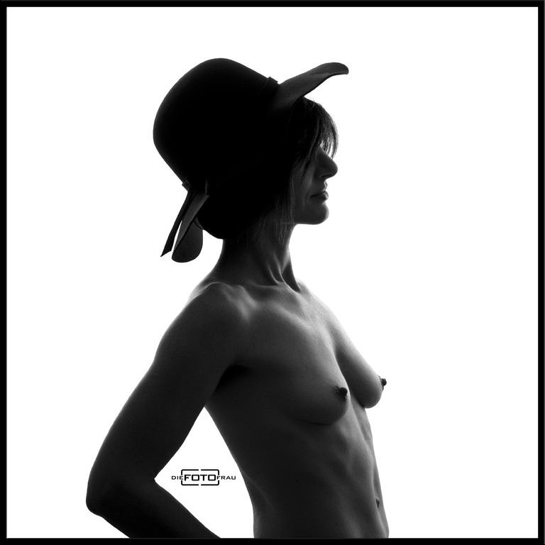 Boudoirfoto im Fotostudio Linz in schwarzweiss einer Dame im Gegenlicht, sie trägt einen Hut