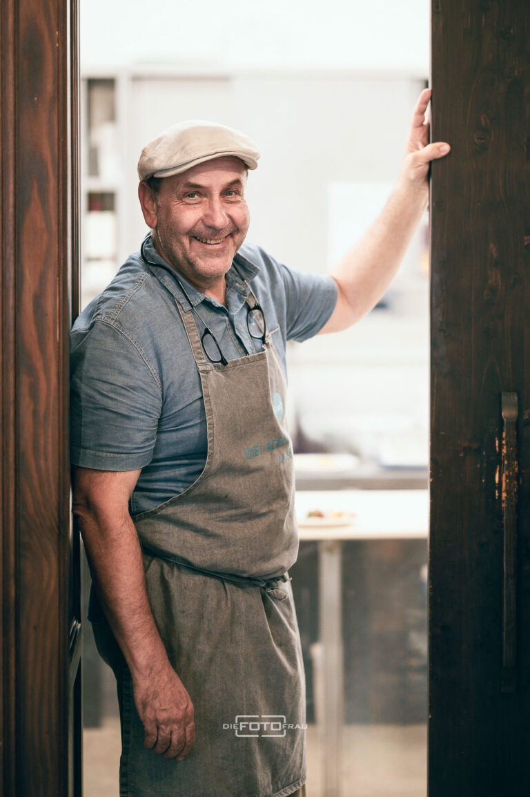 Businessportrait eines Herrn in Arbeitskleidung vor dem Eingang zu einer Betriebskueche