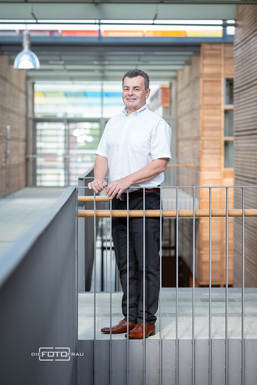 Businessportrait eines Herrn in weisse Hemd vor Metallgelaender in einem Firmengebaeude