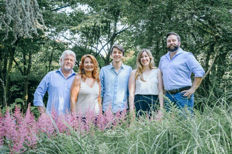 Familienfoto im Botanischen Garten, 5 Personen in Sommerkleidung stehen vor Gräsern, dahinter sieht man Bäume