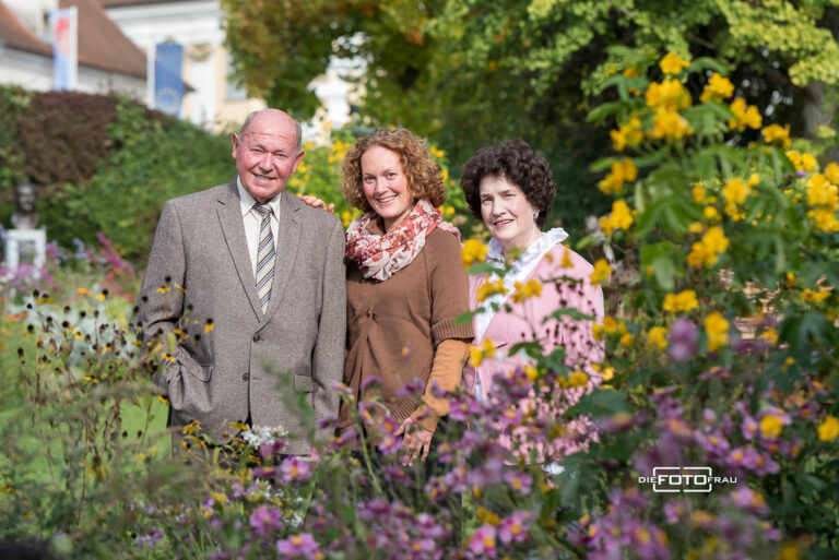 Familienfoto eines älteren Paares mit Tocher vor Blumenkulisse