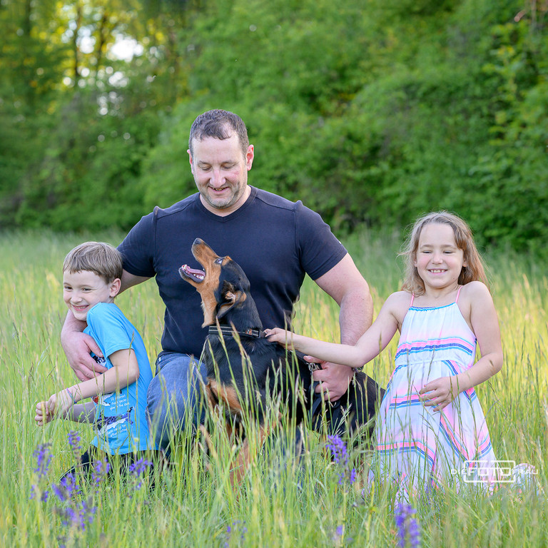Familienfoto mit tobenden Kindern und Hund auf einer Wiese