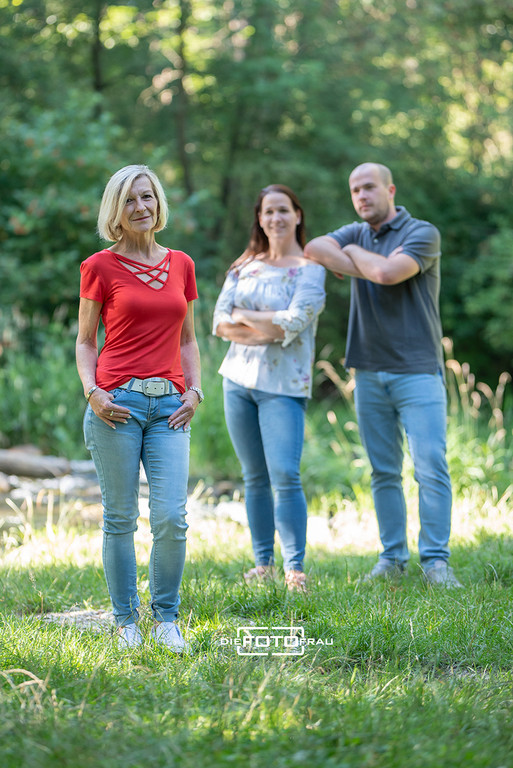 Familienfoto in Parkkulisse, die Mutter steht vorne und die erwachsenen Kinder blicken von hinten auf die Mutter