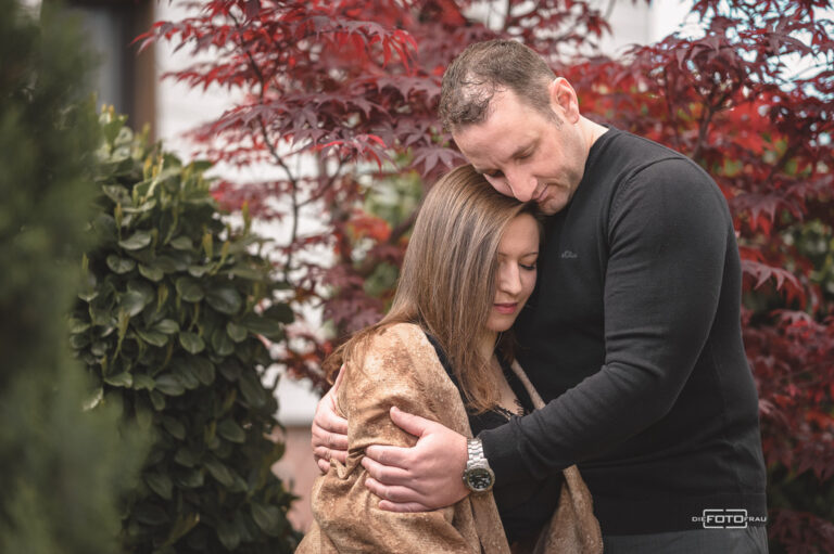 Paarfoto vor herbstlicher Kulisse, der Mann legt die Arme um seine Partnerin