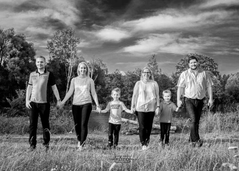 Familienfoto im Panoramastil, die Familie geht nebeneinander Hand in Hand über eine Wiese, schwarzweiss