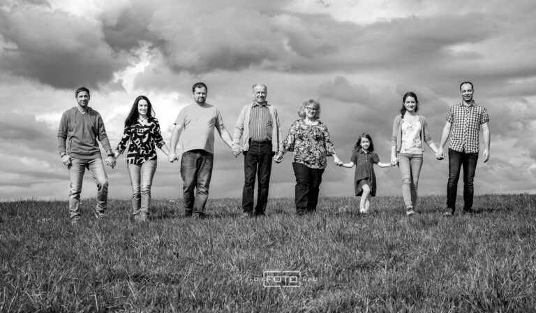 Familienfoto im Panoramastil, drei Generationen gehen Hand in Hand über eine Wiese, schwarzweiss