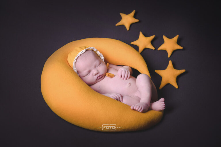Neugeborenenfoto mit Baby welches auf einem gelben Stoffmond liegt, dekoriert mit gelben Sternen