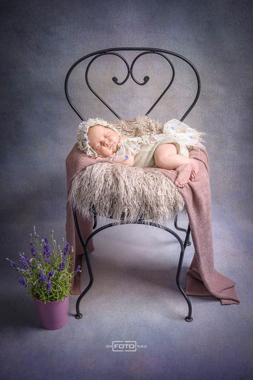 Neugeborenenfoto mit schlafendem Baby, dieses ist auf einem Stuhl in Herzform gebettet