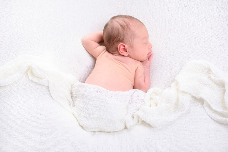 Neugeborenenfoto mit schlafendem Baby auf weissem Untergrund mit weisser Decke