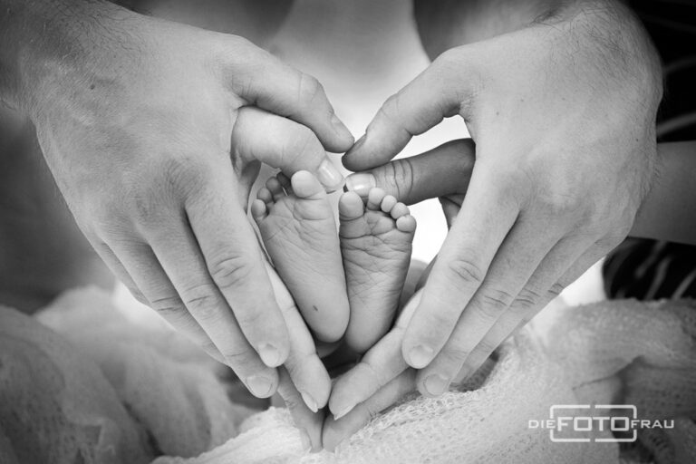 Neugeborenenfoto mit Babyfüssen, die von den Eltern gehalten werden, schwarzweiss