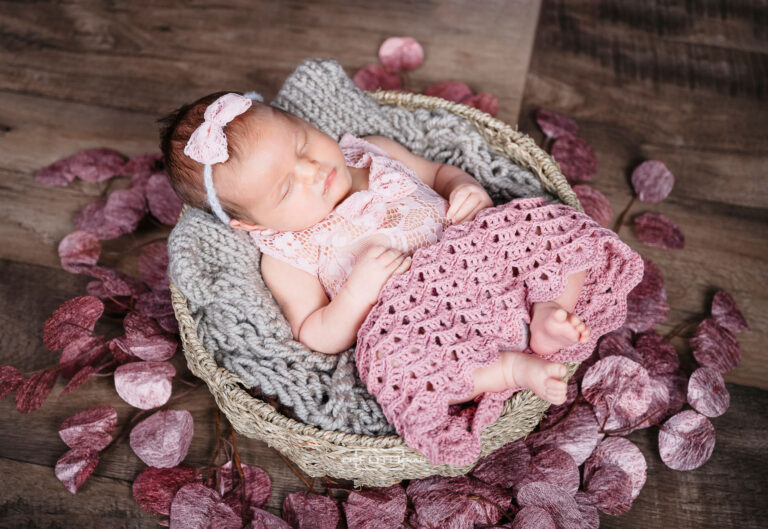 Neugeborenenfoto mit schlafendem Baby in einem rosa handgehäkelten Häkelrock, gebettet in einen Korb und rosa Dekoration