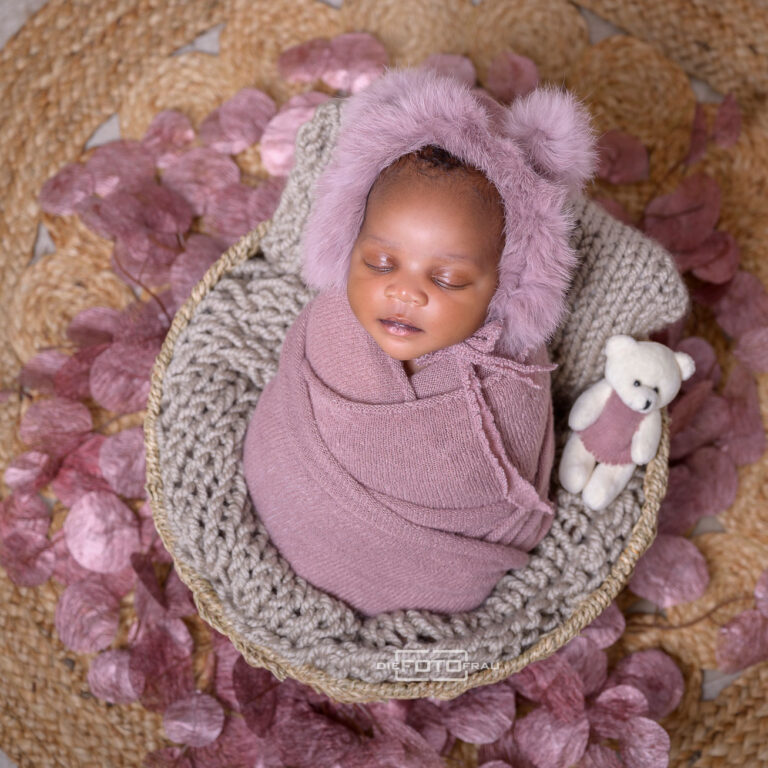 Neugeborenenfoto mit schlafendem Baby in rosa Haube und rosa Pucktuch, gebettet in einen Korb