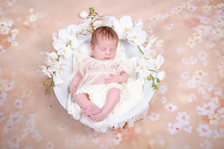 Neugeborenenfoto mit schlafendem Baby in weisser Schale auf Blumendeko