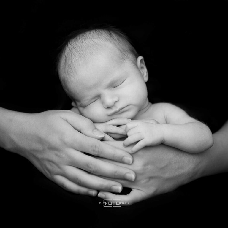 Neugeborenenfoto mit schlafendem Baby in den Händen der Eltern, schwarzweiss