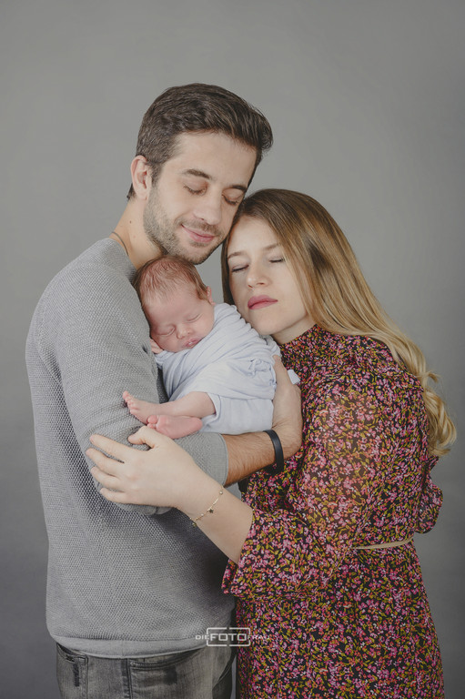 Neugeborenenfoto mit schlafendem Baby, die Eltern umarmen sich und das Kind