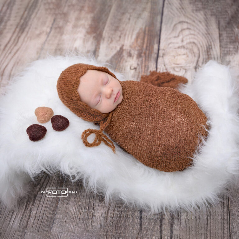 Neugeborenenfoto mit schlafendem Baby auf einer Fellwiege, Holzuntergrund und braunen Herzen