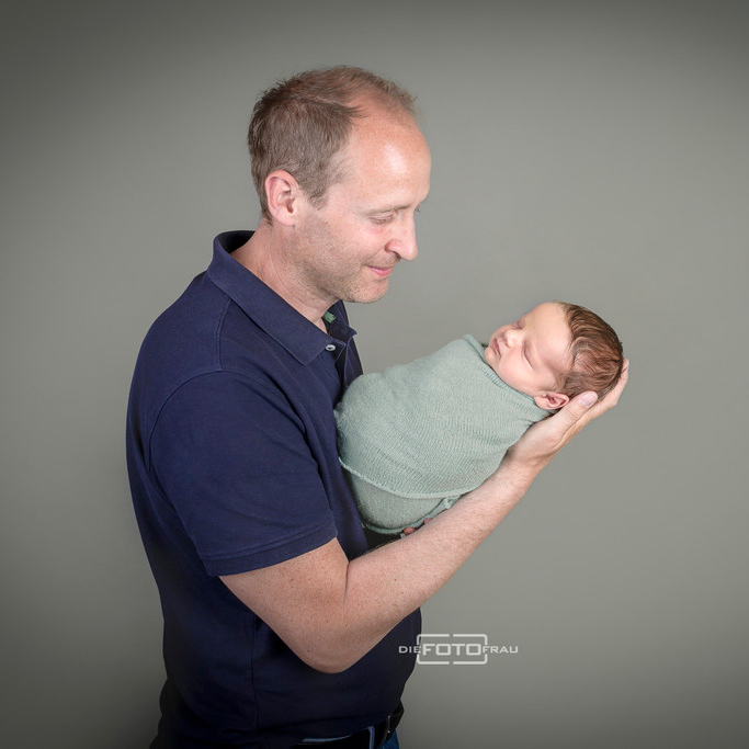 Neugeborenenfoto mit schlafendem Baby in Papas Armen