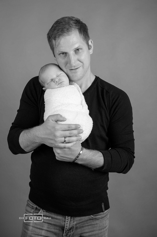 Neugeborenenfoto mit schlafendem Baby in Papas Armen, schwarzweiss