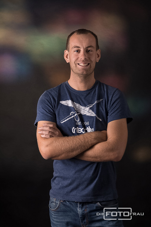 Portraitfoto eines jungen Mannes im Fotostudio Linz für ein Datingportal, der Hintergrund ist bunt und der Herr trägt ein blaues T-Shirt