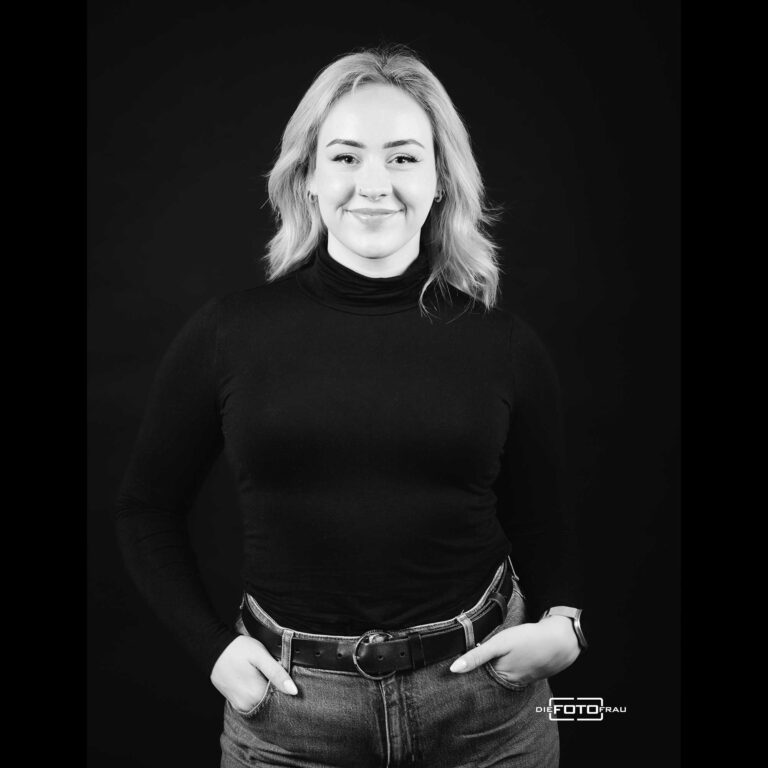Portraitfoto im Fotostudio Linz in schwarzweiss mit Dame direkt in die Kamera blickend, die Haende in der Hosentasche