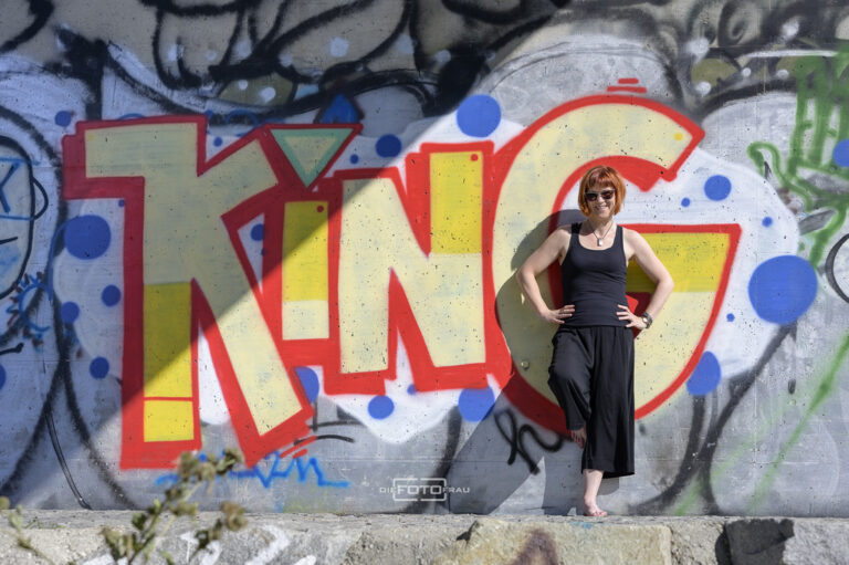Portraitfoto einer sportlichen Dame vor einer bunten Graffitimauer
