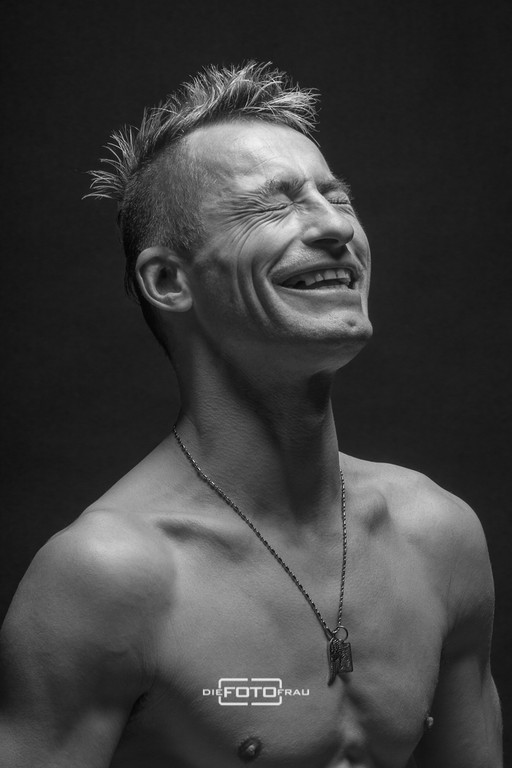 Portraitfoto eines lachenden Mannes mit nacktem Oberkörper in schwarzweiss im Fotostudio Linz