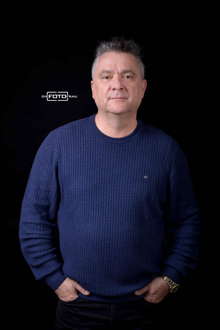 Portraitfoto eines Herrn im blauen Pullover vor schwarzer Kulisse im Fotostudio Linz