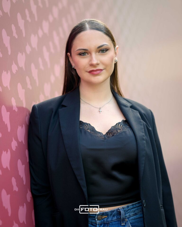 Portraitfoto einer jungen Dame mit stylishem Outfit und Makeup neben einer farbig spiegelnden Wand