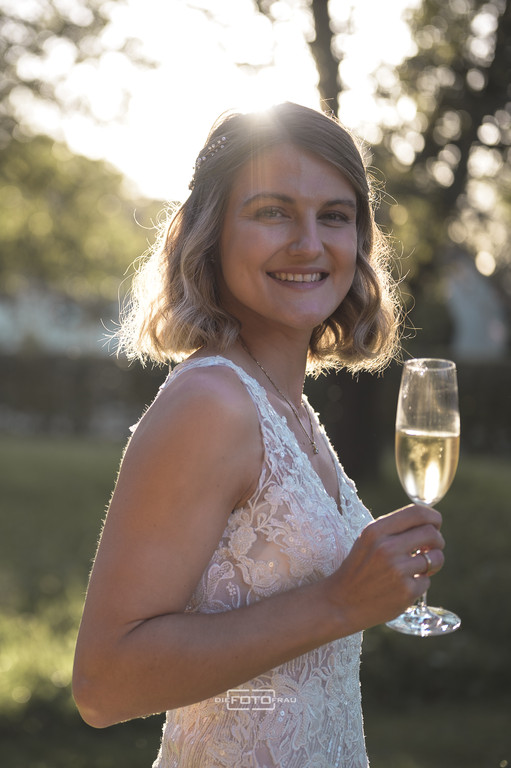 Hochzeitsreportage beim Feiern mit den Gästen, die Braut hält ein Sektglas in der Hand und wird von der Abendsonne angestrahlt