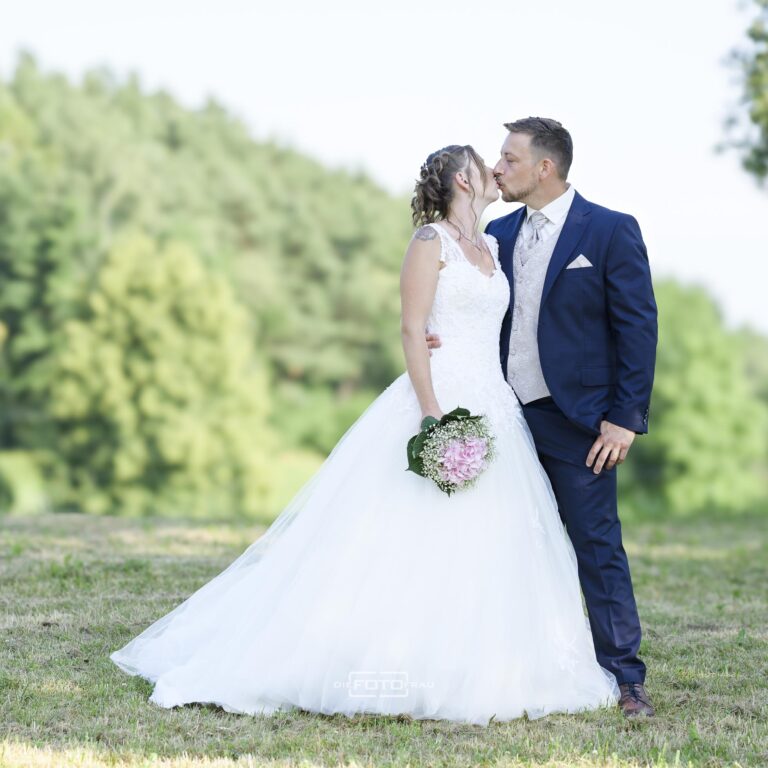 Brautpaar küsst sich beim Fotoshooting bei ihrer Sommerhochzeit im Garten