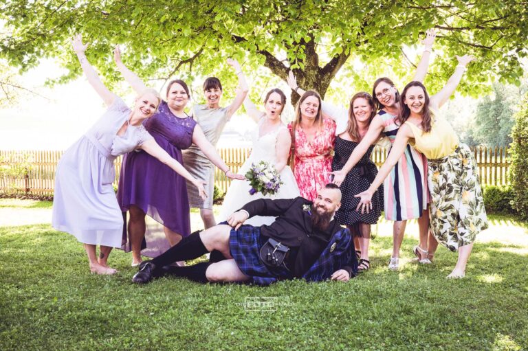 Bräutigam im Kilt wird von den Brautjungfern und der Braut beim Gruppenfoto bejubelt