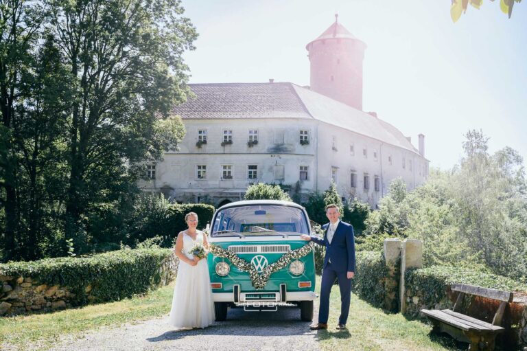 Braut und Bräutigam stehen mit ihrem VW-Bulli vor Schloss Wildberg