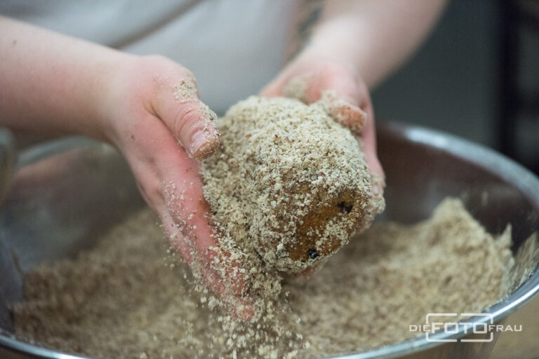 Hände die ein Kletzenbrot mit Nüssen bestreuen