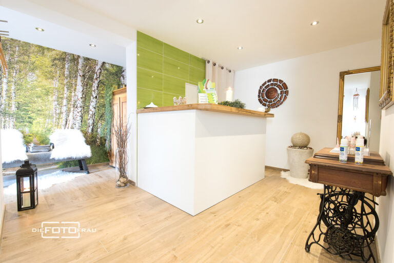 Einrichtung Empfangsbereich Massagesalon mit grüner Wand und Baumtapete
