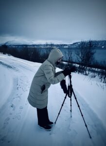 Frau im Daunenmantel in Schneelandschaft mit Kamera auf Stativ