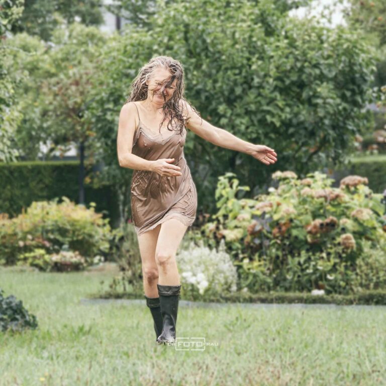 Dame im nassen Neglige läuft bei Regen mit Gummistiefel durch den Garten